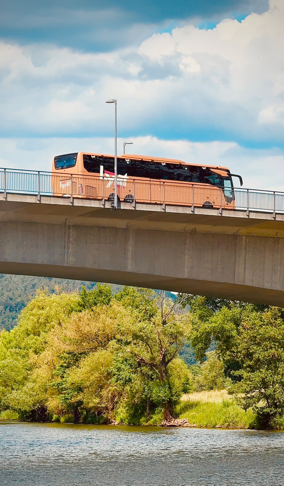 Coach crossing a river bridge with green hills in the background
