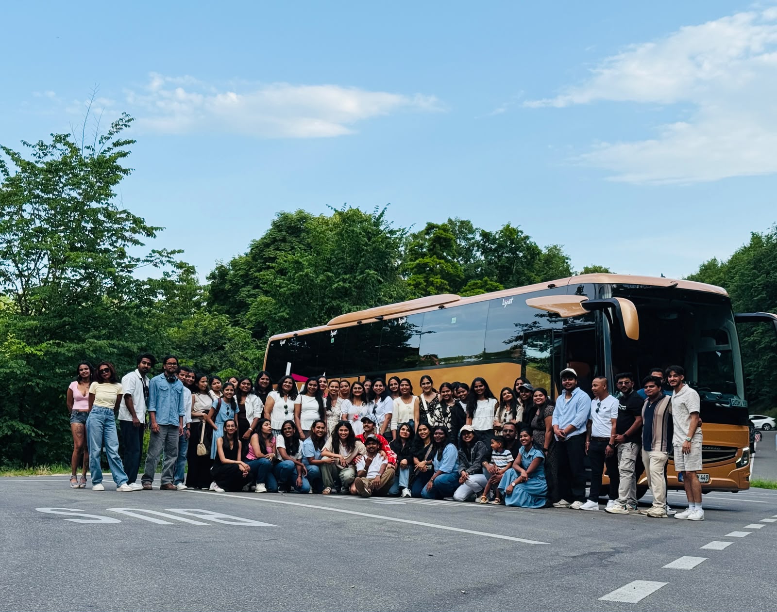 Large tour group beside the gold Lyst coach before departure