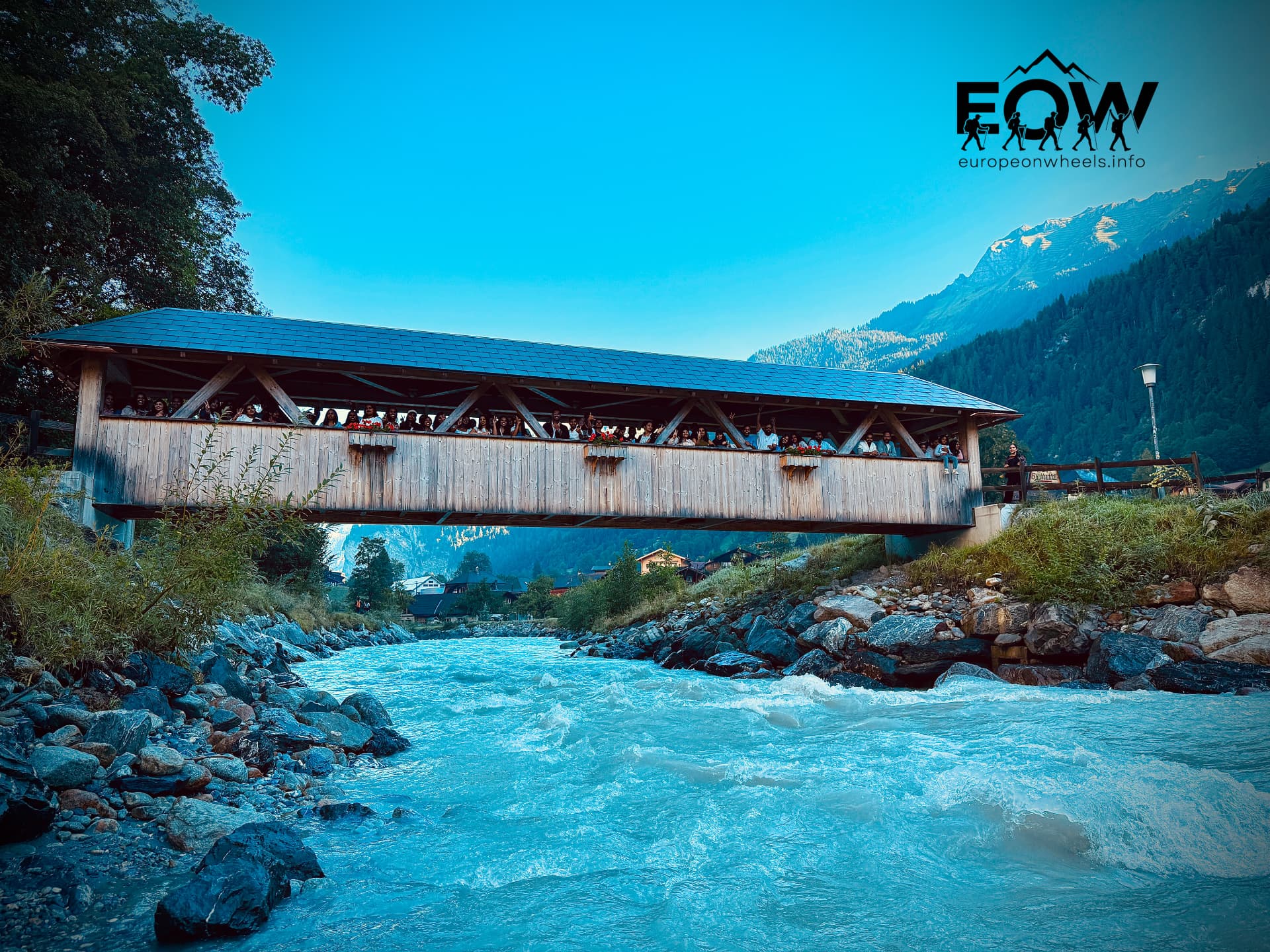Covered wooden bridge over the turquoise river with the Swiss Alps behind